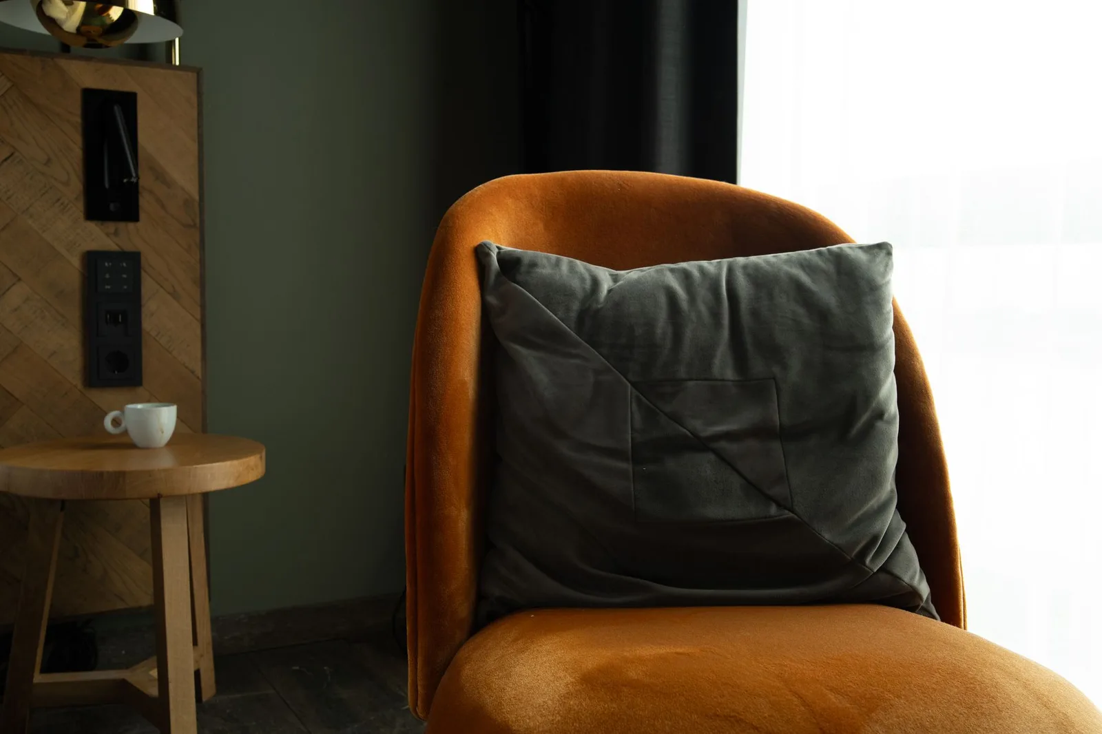 A warm, inviting corner with an orange velvet chair, grey cushion, and a small coffee table in a modern interior setting.