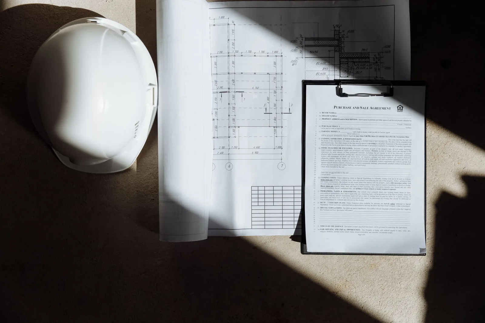 Top view of construction documents and hard hat in sunlight, capturing planning essence.