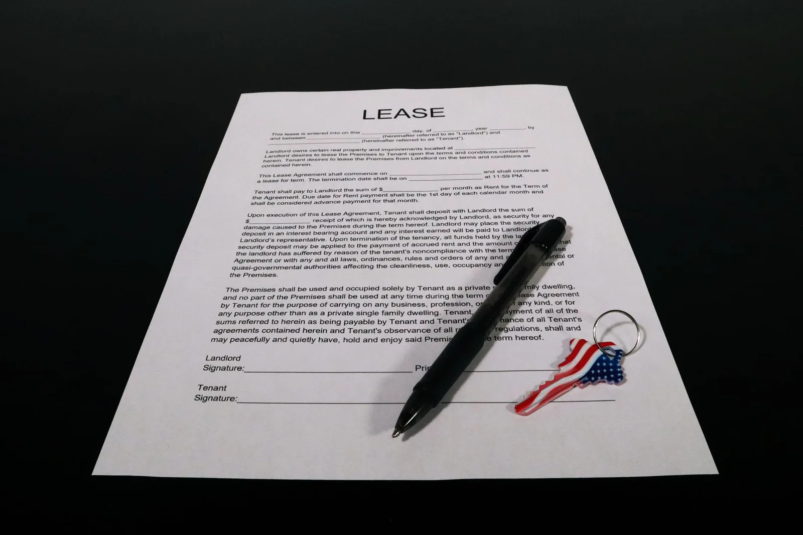 Lease agreement document with pen and American flag keychain on a black table.