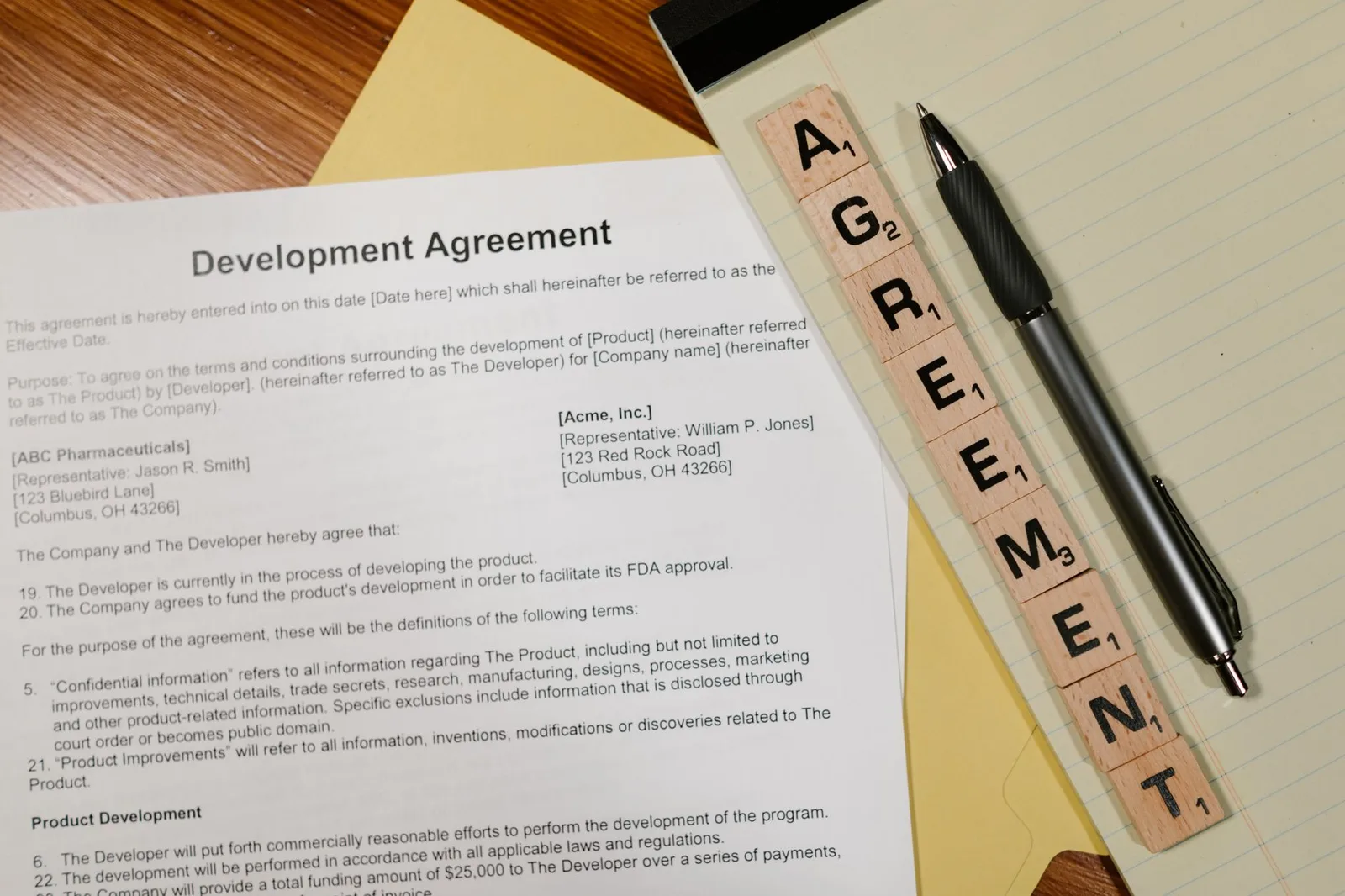 Close-up of a development agreement document with pen and Scrabble tiles spelling 'AGREEMENT.'