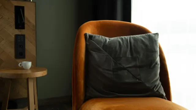 A warm, inviting corner with an orange velvet chair, grey cushion, and a small coffee table in a modern interior setting.