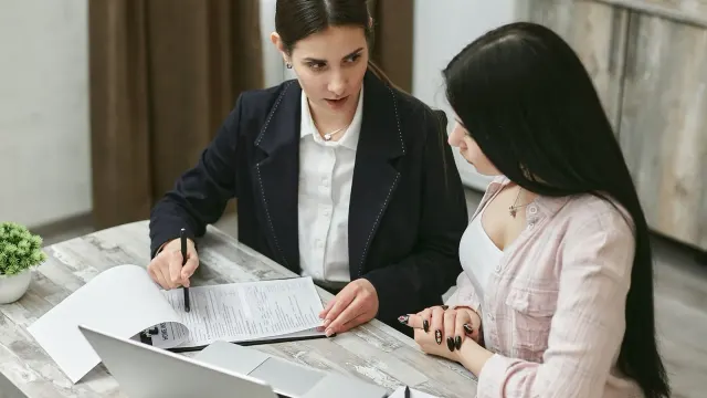 Two businesswomen engaged in a contract discussion at an office table.