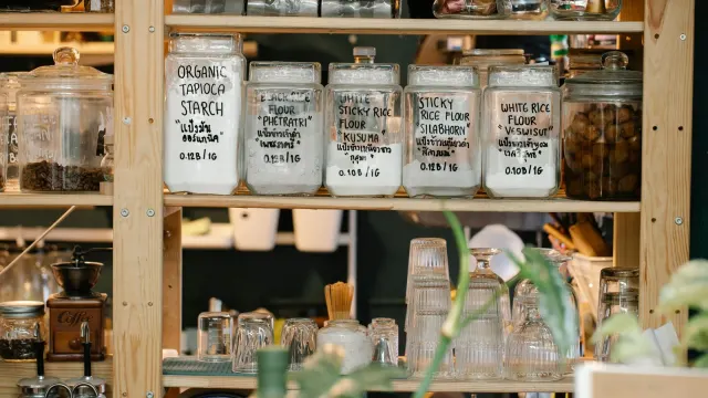 Collection of various glass jars with different dry food and glassware placed on wooden shelf
